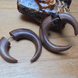 Op de afbeelding: Een paar donkerbruine houten oorpluggen in de vorm van een halve maan. De pluggen zijn gemaakt van hout en hebben een gladde afwerking.