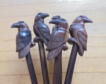 May include: Five wooden raven hair sticks. Each stick features a detailed carving of a raven with black and brown paint accents.