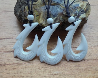 May include: Three white bone fish hook pendants on black cords with white beads. The hooks are carved with intricate designs.
