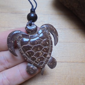 May include: A brown coconut shell turtle pendant necklace. The turtle is carved with detailed shell markings and has a black cord.