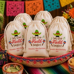 May include: A set of off-white drawstring canvas favor bags featuring a colorful graphic of a sombrero, maracas, and musical notes. The text reads "let the Fiesta begin!" followed by "Amanda's 40th Birthday" and "2025" in red and brown ink.
