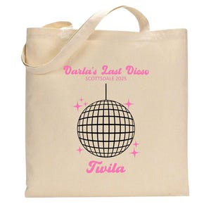 May include: A white canvas tote bag with a pink and black design. The text on the bag reads "Darla's Last Disco Scottsdale 2025" and "Twila". A black and white disco ball is in the centre of the design.