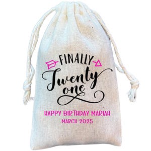 Puede incluir: Una bolsa de tela blanca con el texto "FINALLY TWENTY ONE" en letras negras y flechas rosas. El texto "HAPPY BIRTHDAY MARIAH MARCH 2025" tambi&eacute;n est&aacute; impreso en la bolsa.