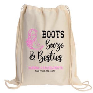 May include: A beige drawstring backpack featuring a pink graphic of a cowboy boot with flowers. The text reads BOOTS Booze & Besties in black and pink, followed by CARISSA'S BACHELORETTE and NASHVILLE, TN - 2025 in pink and black lettering.