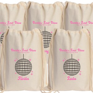 May include: Five white drawstring bags with a pink disco ball graphic and the text "Darla's Last Disco Scottsdale 2025". Two bags have the names "Twila" and "Zula" printed below the graphic.