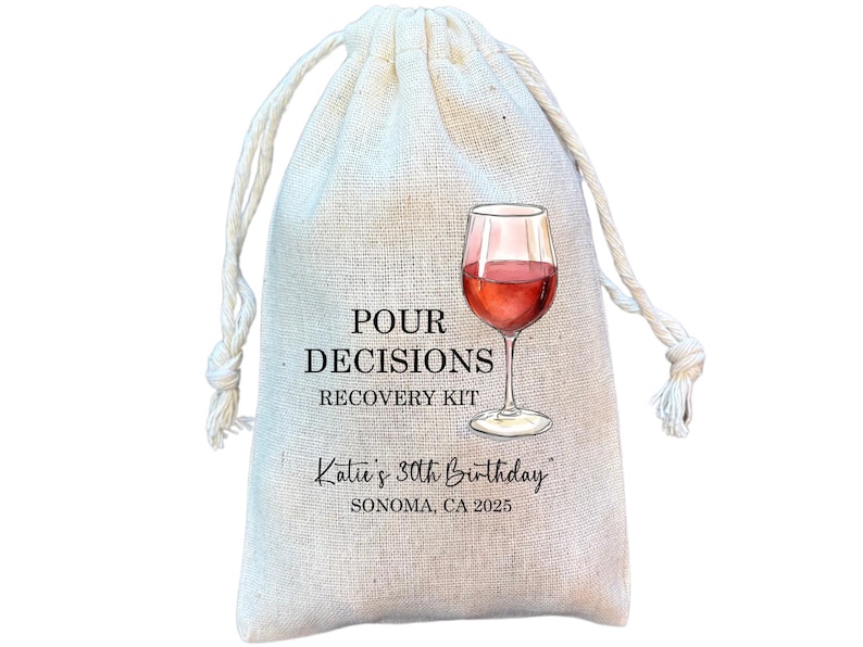 May include: A beige drawstring bag with the text "POUR DECISIONS RECOVERY KIT" and a watercolor illustration of a wine glass filled with red wine. The bag also includes the text "Katie's 30th Birthday, Sonoma, CA 2025."
