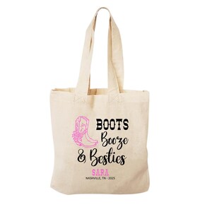 May include: A beige canvas tote bag featuring a pink graphic of a cowboy boot and the black text "BOOTS Booze & Besties". Below the text, the name "SARA" is printed in pink, followed by the black text "NASHVILLE, TN - 2025" on the front.