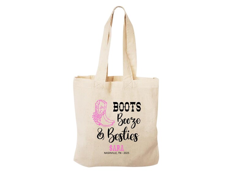 May include: A beige canvas tote bag featuring a pink graphic of a cowboy boot and the black text "BOOTS Booze & Besties". Below the text, the name "SARA" is printed in pink, followed by the black text "NASHVILLE, TN - 2025" on the front.