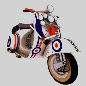 May include: A white, red and blue scooter clock with a target design. The clock has a white face and black hands.
