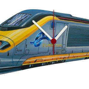 May include: A novelty clock in the shape of a high-speed train. The clock face is designed as a yellow and blue train with the Eurostar logo. The clock hands are white. A decorative item for the home.