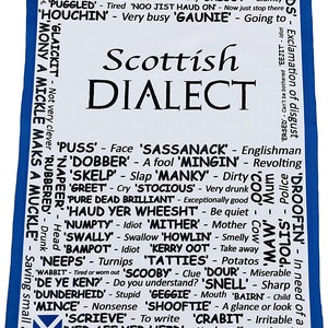 May include: A white tea towel with a blue border features a list of Scottish words and their meanings. The words are written in black text and are arranged in a grid pattern. The Scottish flag is in the bottom left corner of the towel.