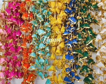 May include: A vibrant display of hanging fabric decorations in pink, orange, teal, yellow, blue, green, and white. Each ornament features gold trim. The word "Vasavi" is written in cursive in the center of the image.
