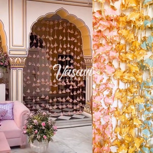 May include: A decorative doorway with pink, gold, and blue tassel garlands. The tassels are made of fabric and have a metallic sheen. The garlands are hung from the ceiling and create a festive atmosphere.