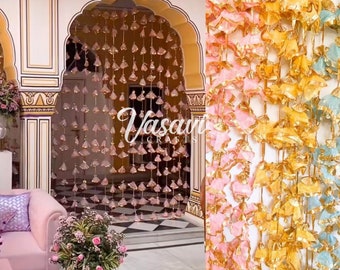 May include: A decorative doorway with pink, gold, and blue tassel garlands. The tassels are made of fabric and have a metallic sheen. The garlands are hung from the ceiling and create a festive atmosphere.
