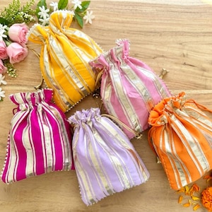 May include: An assortment of colorful drawstring pouches in shades of yellow, pink, orange, purple, and fuchsia, with vertical silver stripes. The pouches are arranged on a wooden surface, with floral accents.