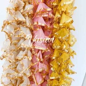 Peut inclure: Trois brins de guirlande en tissu décoratif avec une bordure dorée. La guirlande est faite de couches de tissu transparent en blanc, rose et jaune.