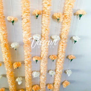 May include: A wall decorated with garlands of peach-colored fabric flowers and white fabric flowers. The garlands are strung on white thread and hang from the ceiling. The text "Vasan Crafts" is visible in the center of the image.