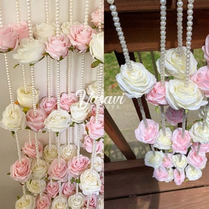 Può includere: Una ghirlanda di rose artificiali rosa e bianche infilate su una collana di perle. La ghirlanda è appesa a un corrimano di legno.