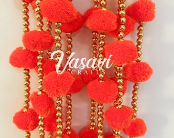 May include: Decorative garland featuring vibrant orange pom-poms and golden beads. The pom-poms are evenly spaced along strands of golden beads, creating a festive and eye-catching design. The garland is suitable for various decorative purposes.