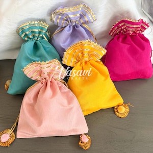 Peut inclure: Plusieurs sacs à cordon colorés en rose, jaune, turquoise, violet et fuchsia. Chaque sac est orné d'une bordure dorée et d'un pompon assorti. Les sacs sont faits d'un matériau doux et soyeux.
