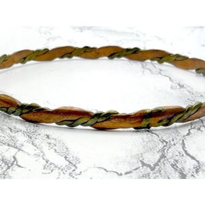 May include: A copper-toned bangle bracelet with a twisted design. The bracelet features a combination of copper and green-toned metal, creating a textured and eye-catching pattern. The bracelet is a simple, yet elegant piece of jewelry.