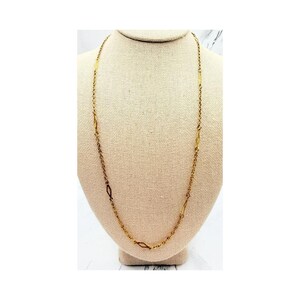May include: A long gold-tone chain necklace featuring a series of delicate, elongated diamond-shaped links interspersed along the length of the chain. The necklace has a polished metallic finish and a simple, continuous design without a visible pendant.