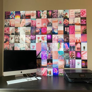 Op de afbeelding: Een zwarte desktopcomputer met een wit toetsenbord en een zwarte printer op een zwart bureau. De muur achter het bureau is bedekt met een roze en witte collage van foto's.