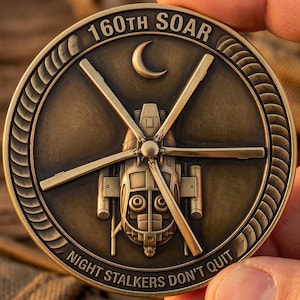May include: A circular bronze-toned challenge coin featuring a relief of a helicopter in the center, a crescent moon above, and the text 160TH SOAR and NIGHT STALKERS DON'T QUIT embossed along the outer rim with a rope-like border design.