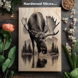 May include: A wooden art piece featuring a detailed illustration of a moose drinking from a lake, with mountains and trees in the background. The artwork is on a light-colored wood surface, with the text "Hardwood Slices..." at the top.
