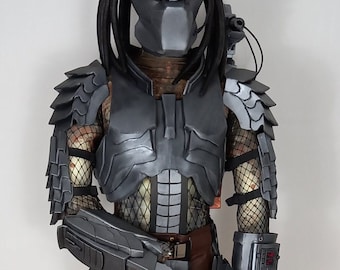 Pode incluir: Uma figura de ação Predator cinza com um corpo detalhado e articulado, incluindo um capacete, armadura de peito e armas. A figura está em pose com uma arma na mão.