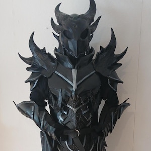 May include: A full-body suit of black fantasy armor featuring a horned helmet, spiked shoulder pauldrons, gauntlets, and greaves. The chest piece displays intricate silver-toned detailing, and a dark fabric loincloth hangs from the waist belt.