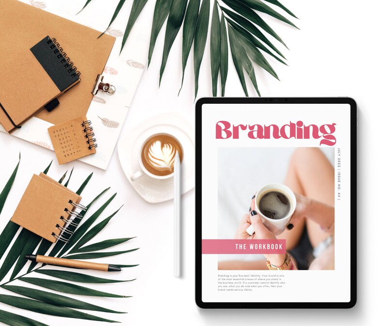 May include: A digital tablet displaying a branding workbook with the title "Branding" in pink text. The workbook cover features a photo of a person holding a cup of coffee. The text "The Workbook" is below the photo. The text "#1 ON INSPIRATION | EBOOK AND APP" is on the right side of the image.