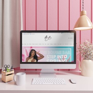 May include: A computer screen displaying a website with the text "The Bougie Bar Step Into Spring" on a pink and blue background. The website is for a clothing store and features a model wearing a one-piece swimsuit.
