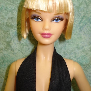 May include: A doll with a blonde bob hairstyle and blue eyes. The doll is wearing a black halter top. The doll has pink lipstick and long eyelashes. The doll's skin is a light peach colour.
