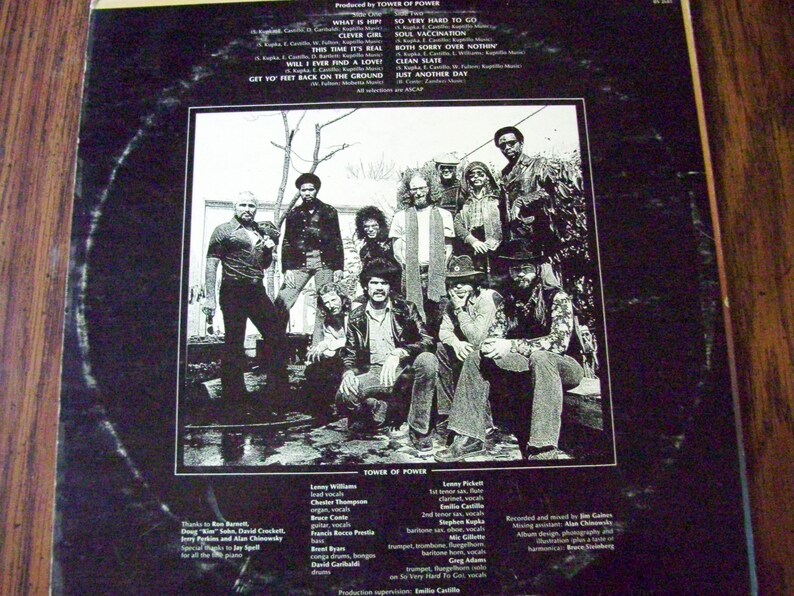 Pu&ograve; includere: Una foto in bianco e nero di una band, Tower of Power, con i membri della band in piedi davanti a un albero. I membri della band indossano tutti abiti casual e hanno i capelli lunghi. La foto &egrave; dalla copertina posteriore di un disco in vinile.