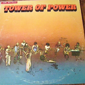 Pu&ograve; includere: Una copertina di un album in vinile vintage con una band chiamata "Tower of Power" con uno sfondo di tramonto e un gruppo di musicisti che suonano strumenti.