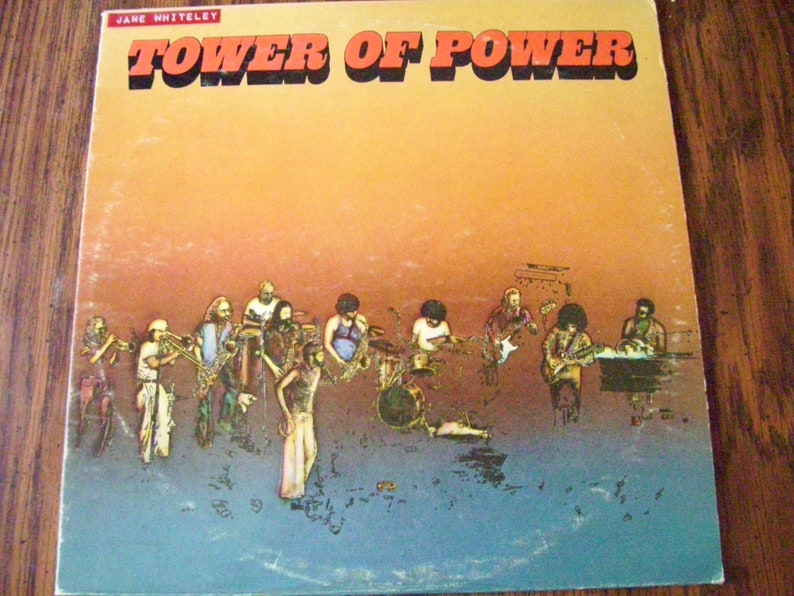 Pu&ograve; includere: Una copertina di un album in vinile vintage con una band chiamata "Tower of Power" con uno sfondo di tramonto e un gruppo di musicisti che suonano strumenti.