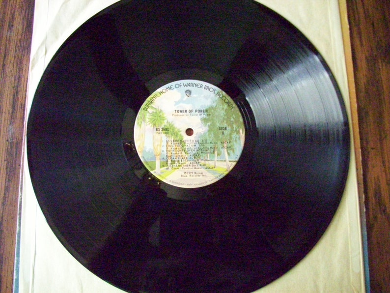 Pu&ograve; includere: Disco in vinile nero con un'etichetta bianca. L'etichetta presenta un'immagine di palme e un edificio con il testo "Tower of Power" e "Warner Bros. Records".
