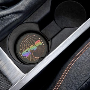 Puede incluir: Un portavasos de coche negro con un posavasos de colores arcoíris con la palabra "STSS" en una fuente estilizada.