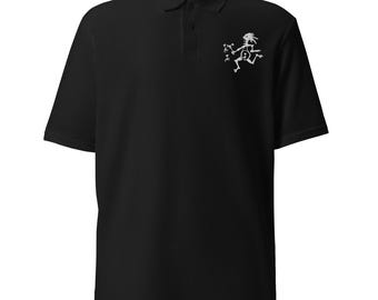 Puede incluir: Un polo negro de manga corta con un gráfico blanco de una figura estilizada de Kokopelli en el pecho izquierdo. La prenda cuenta con un cuello clásico, una tapeta con tres botones y un dobladillo recto, ofreciendo un diseño sencillo.