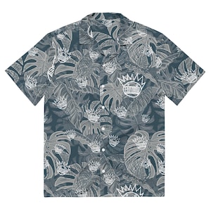 May include: Short-sleeved button-down shirt with a tropical leaf pattern in shades of gray and white. The shirt features a repeating crown graphic. The shirt has a classic collar and white buttons.