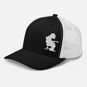 May include: Black and white trucker cap with a curved peak. The front panel is black with a white embroidered design of a person playing a stringed instrument. The back is white mesh.