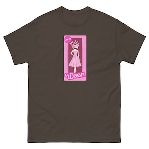 Op de afbeelding: Een bruin t-shirt met een roze afbeelding van een cartoonfiguur dat een roze jurk en een kroon draagt. De afbeelding zegt "LMLYP" en "Ween".