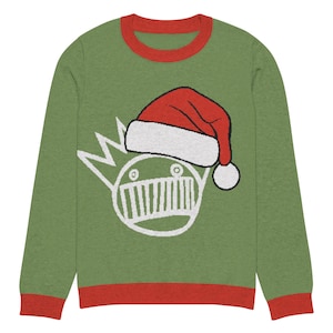 Peut inclure: Pull de Noël vert à manches longues avec bordures rouges au col et aux poignets. Le pull présente un motif blanc d'une couronne et d'un visage portant un bonnet de Père Noël. Le bonnet est rouge avec une bordure blanche et un pompon blanc.