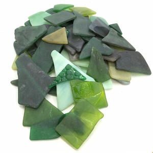May include: A collection of irregularly shaped glass pieces in various shades of green, from light mint to deep forest. Some pieces are translucent, others opaque, creating a textured, mosaic-like appearance. The pieces are scattered against a white background.