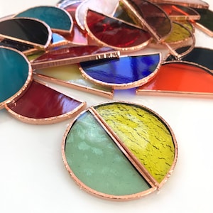 May include: A set of stained glass suncatchers in various colors and patterns, including green, yellow, blue, red, and black. The suncatchers are made of glass and have a copper foil edging.