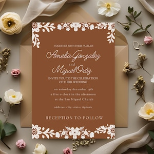 May include: A wedding invitation with a brown background and white floral accents. The invitation includes the names Amelia Gonzalez and Miguel Ortiz, along with the wedding details. The invitation is surrounded by flowers and greenery.