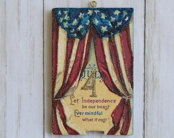 Puede incluir: Una decoración de estilo vintage para el 4 de julio con cortinas de tela roja, blanca y azul y un '4' de purpurina dorada en el centro. El texto dice 'Let Independence be our boast. Ever mindful what it cost.'