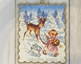 May include: Vintage Christmas ornament with a winter scene. It features a deer, angel, and rabbit in a snowy forest. The ornament has a gold glitter border and the words "CHRISTMAS WISHES".