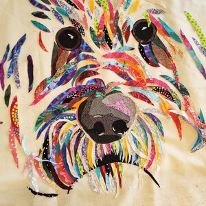 Pode incluir: Um retrato de c&atilde;o de tecido patchwork colorido com nariz e olhos pretos. O tecido &eacute; cortado em tiras longas e costurado para criar um efeito texturizado e em camadas.